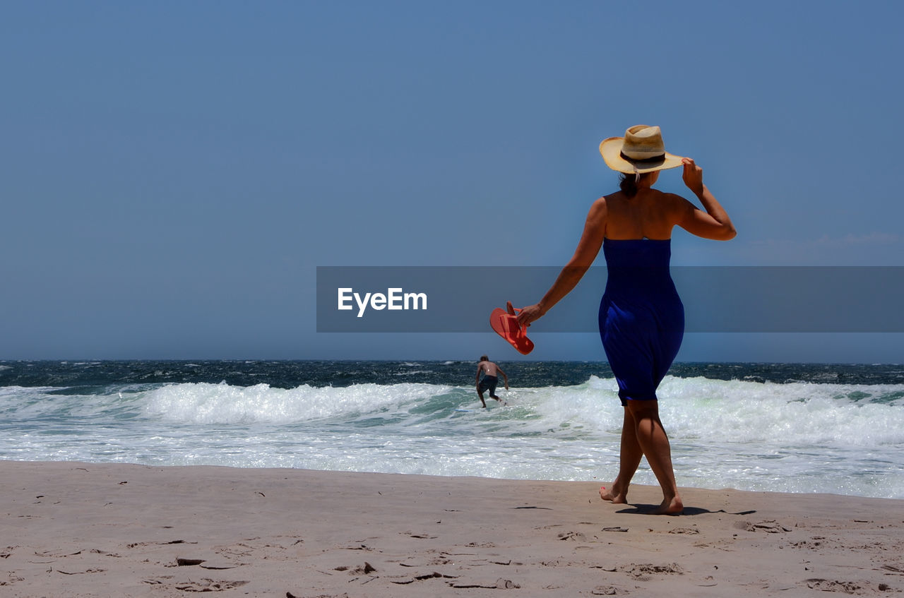 Rear view of woman walking at sea shore against sky