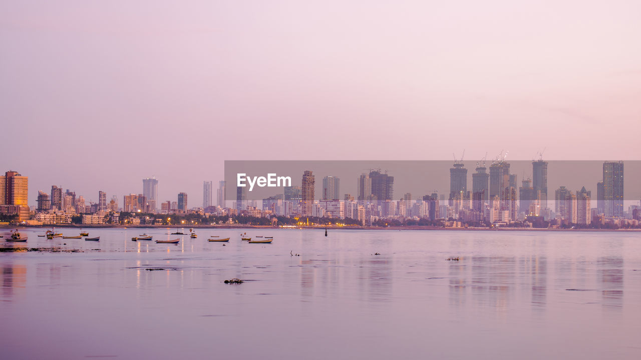 Sea by buildings against sky during sunset