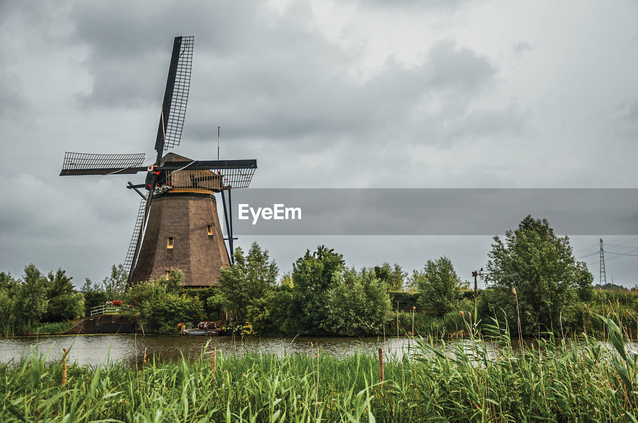 Windmill with bushes aside canal in a cloudy day at kinderdijk. a polder the country of netherlands.