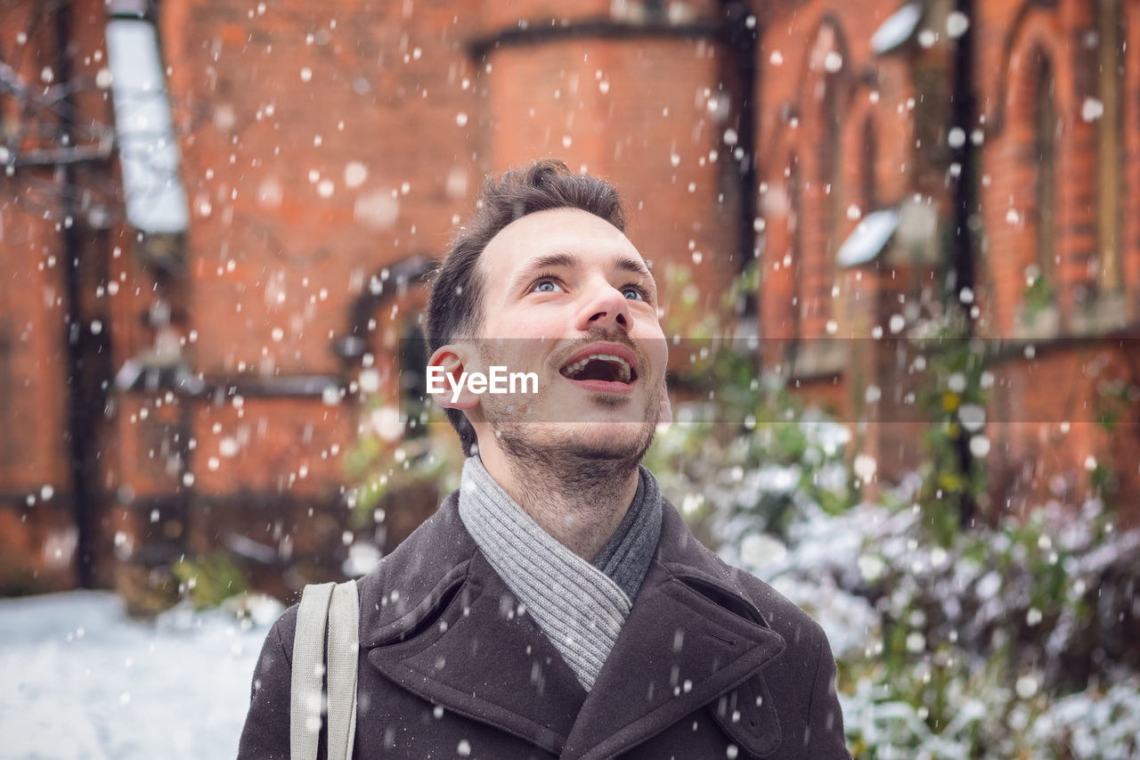 Mid adult man with mouth open looking up during snowfall