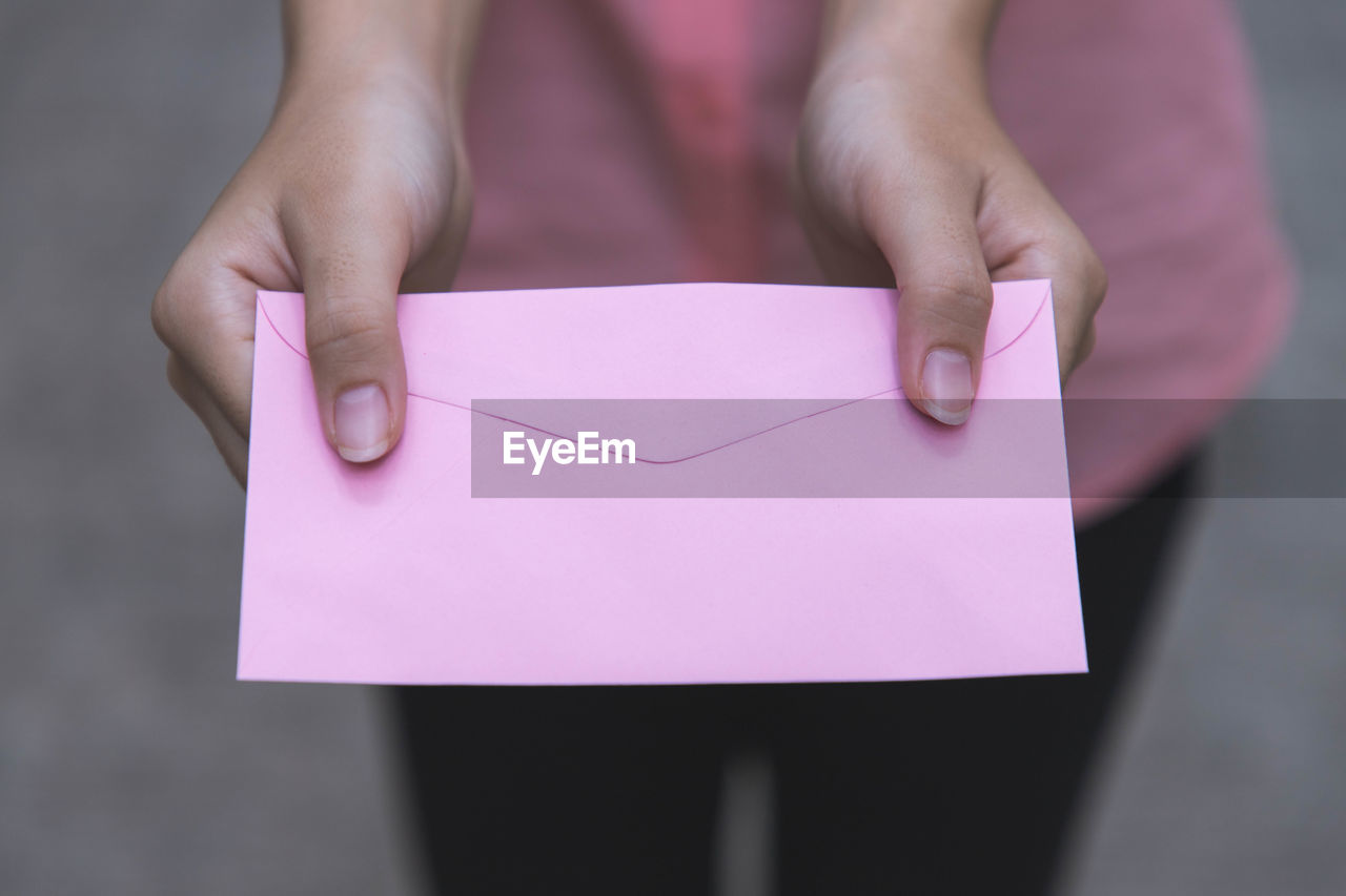 Midsection of woman giving pink envelope