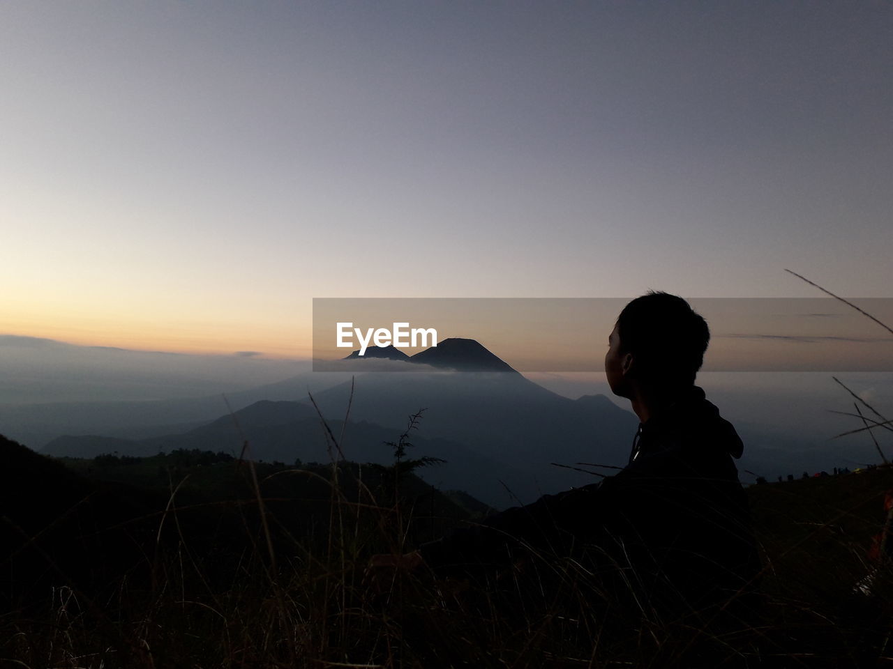 SIDE VIEW OF SILHOUETTE WOMAN SITTING ON LAND AGAINST SKY