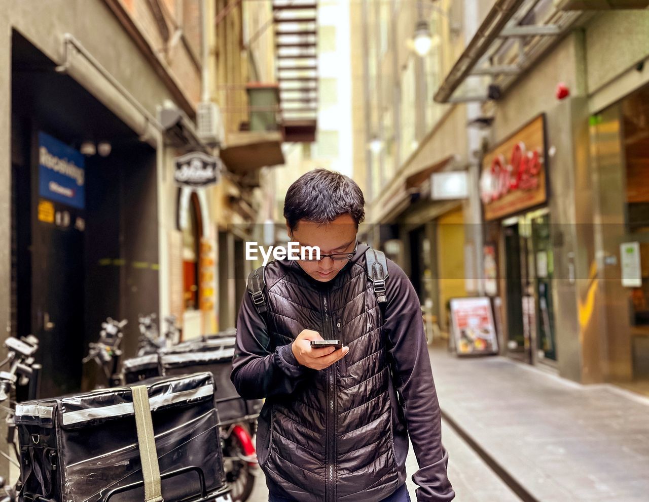Portrait of young asian man using mobile phone in alley against buildings in the city.