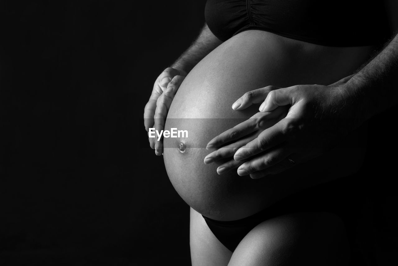 Midsection of pregnant woman touching her belly against black background