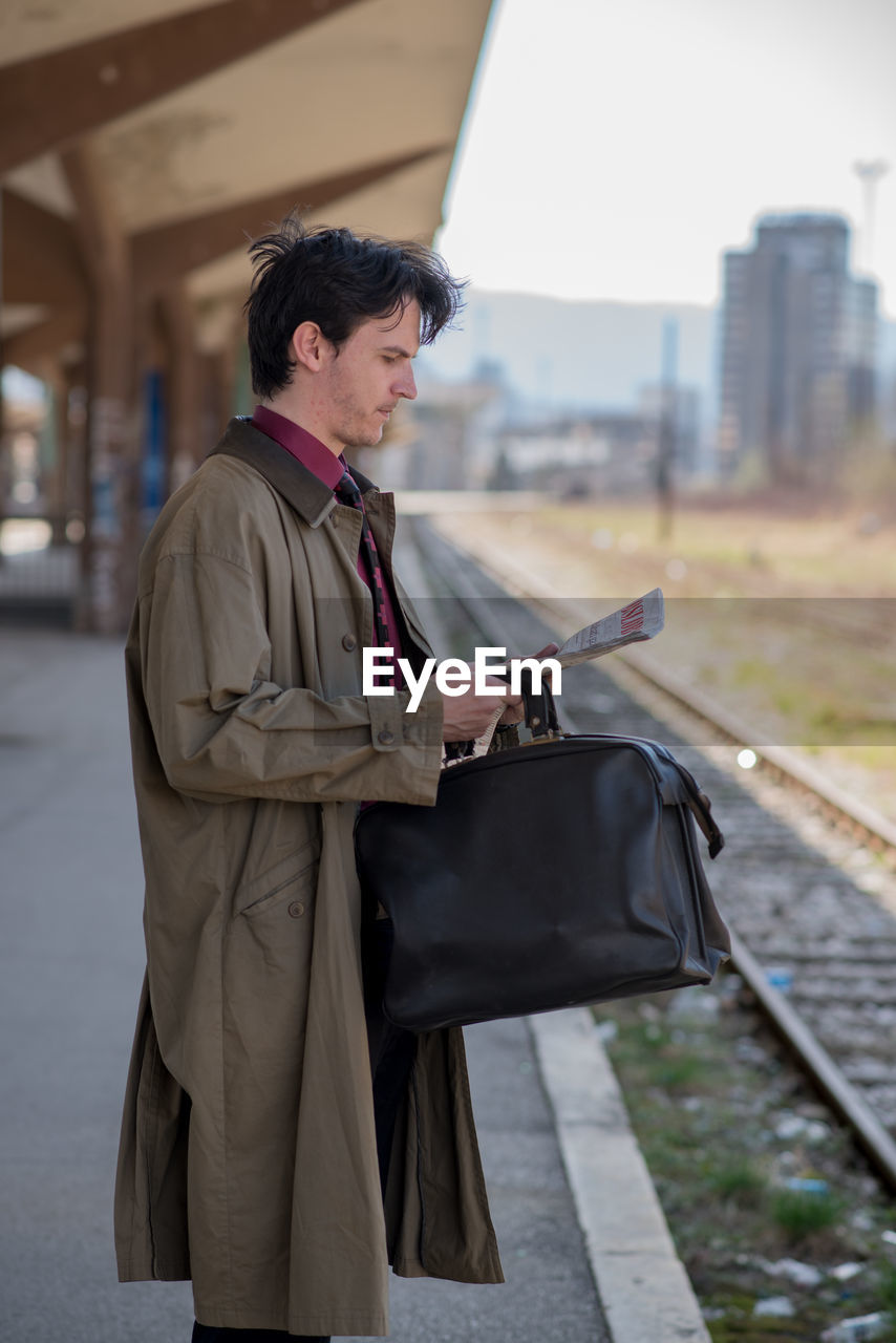 Side view of businessman reading newspaper while standing on platform