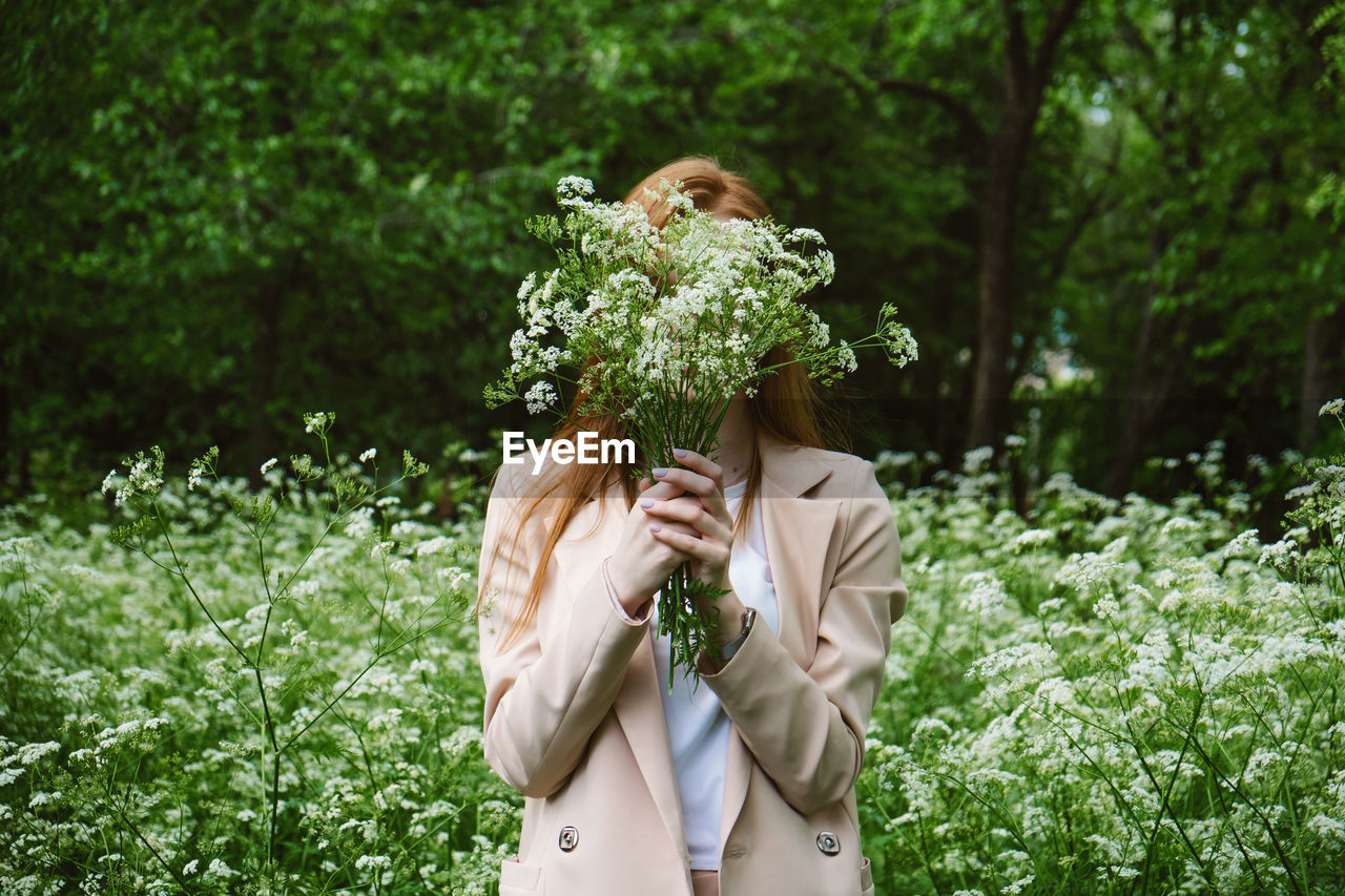 Young woman holding flower while standing by tree