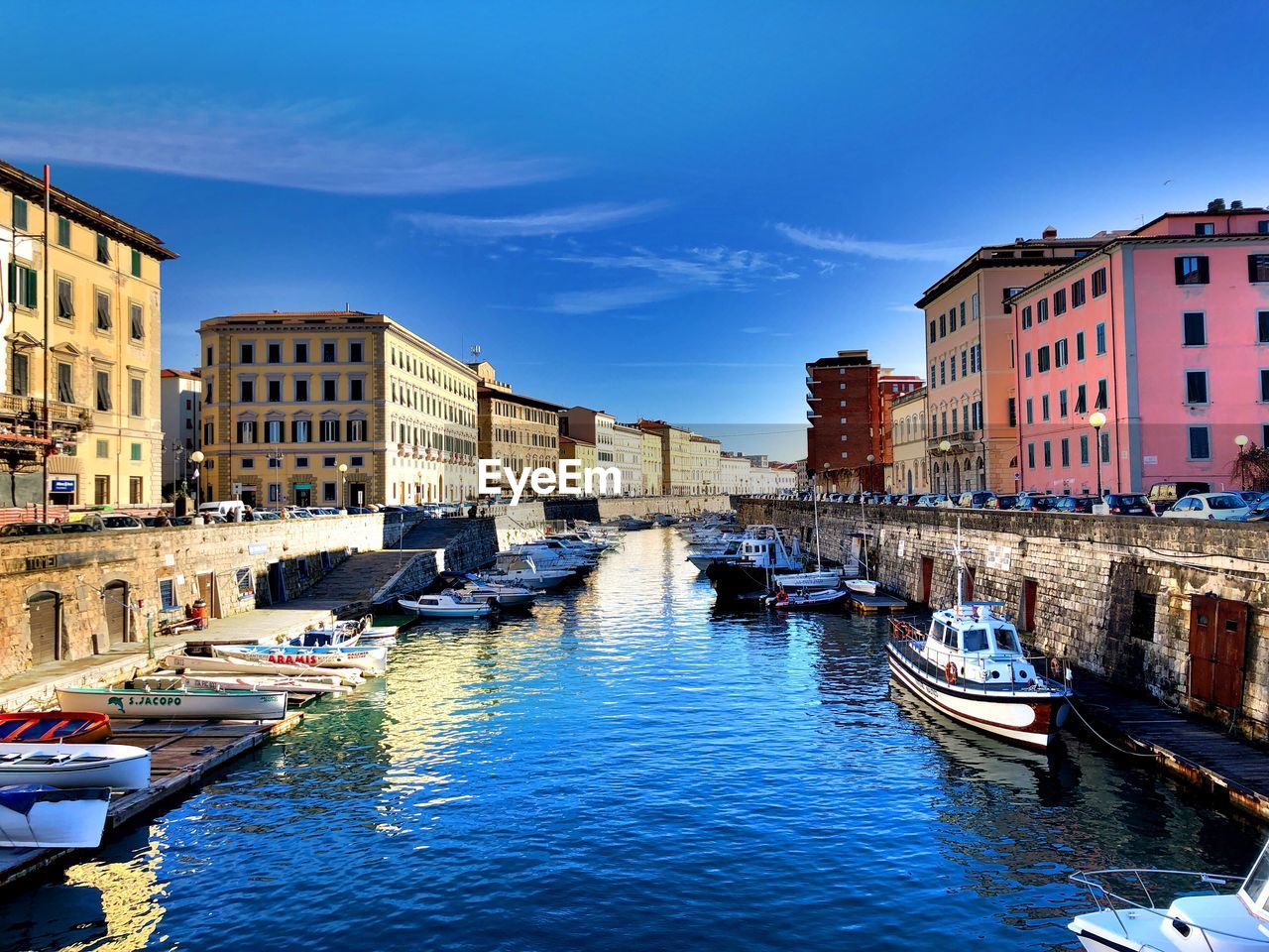 Boats moored in canal amidst buildings in city against sky