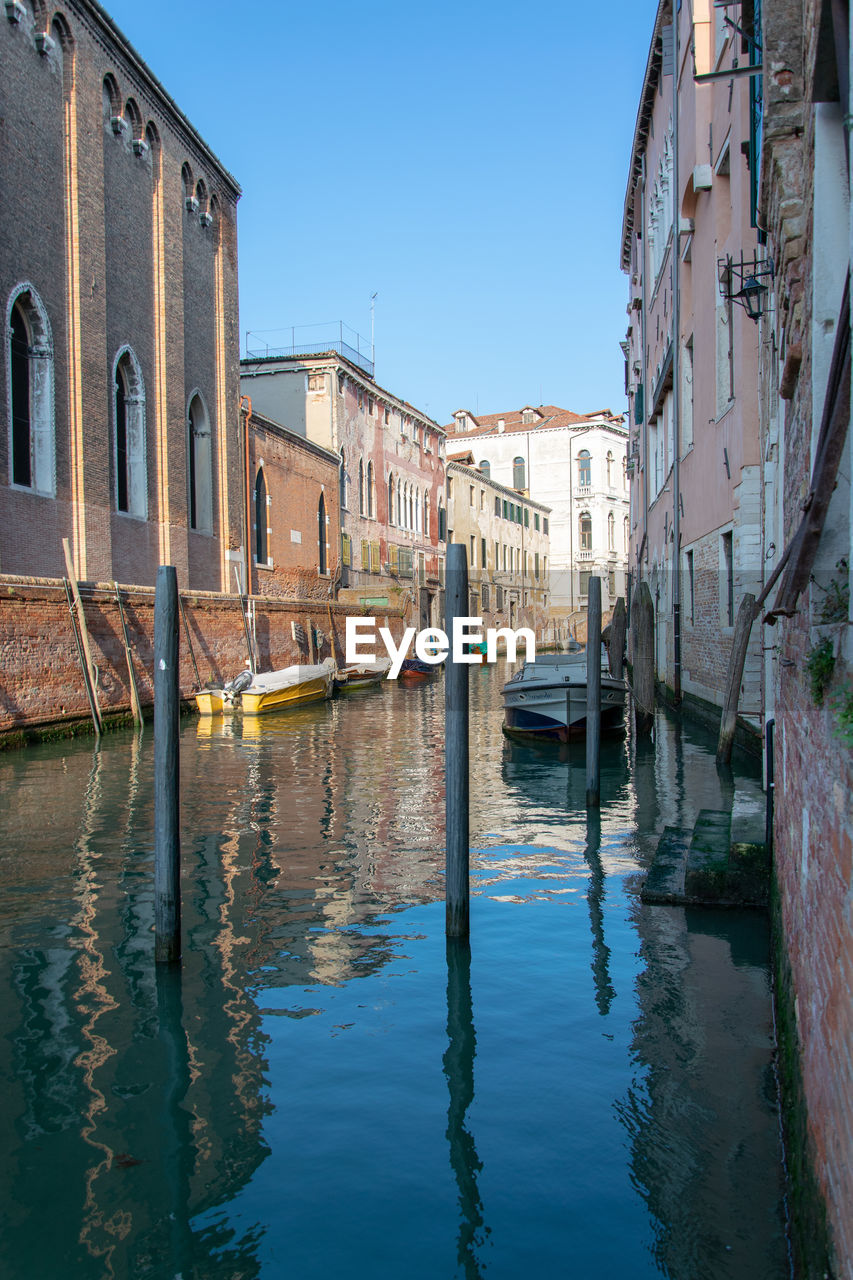 Canal amidst buildings against clear blue sky