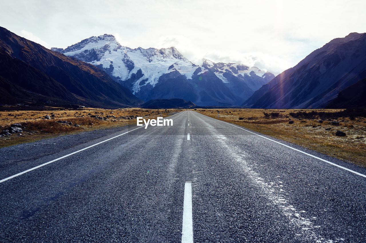 Empty road leading towards snowcapped mountain against sky