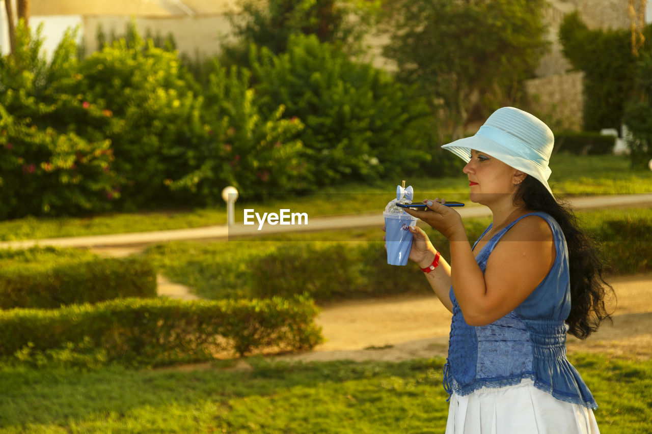 side view of young woman drinking water while standing against trees