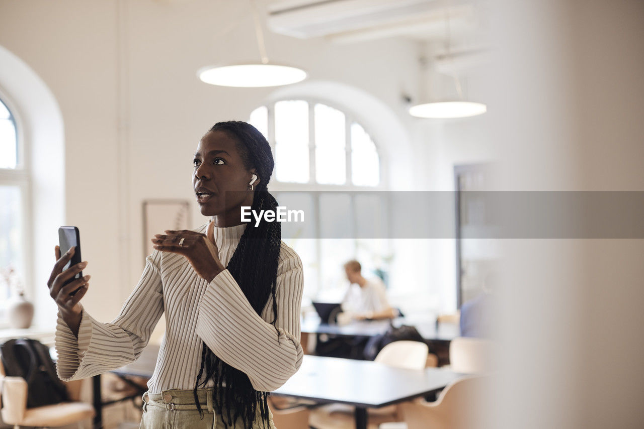 Businesswoman looking away while talking on video call through smart phone at office