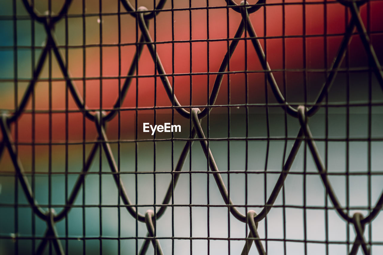 FULL FRAME SHOT OF CHAINLINK FENCE AGAINST BLURRED BACKGROUND