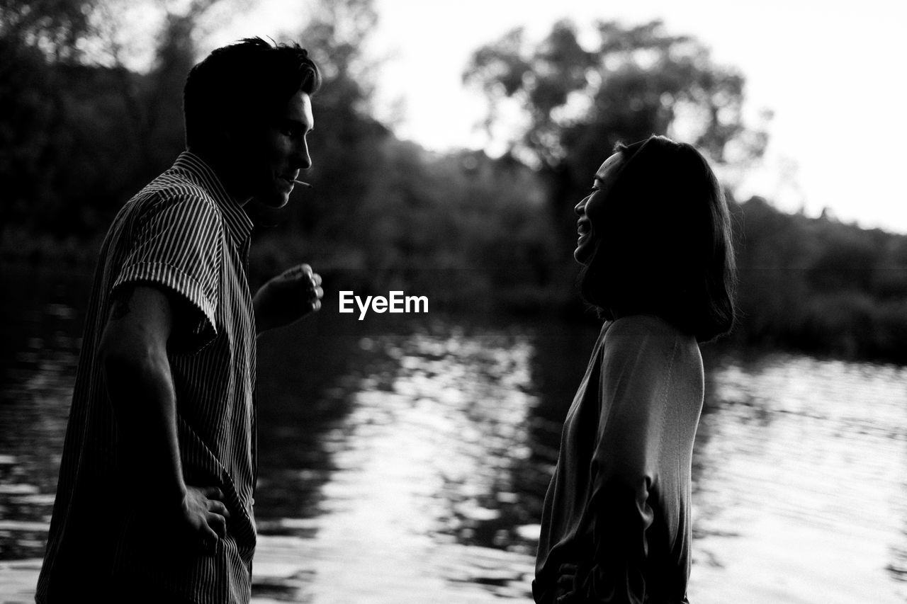 SIDE VIEW OF TWO PEOPLE STANDING ON LAKE