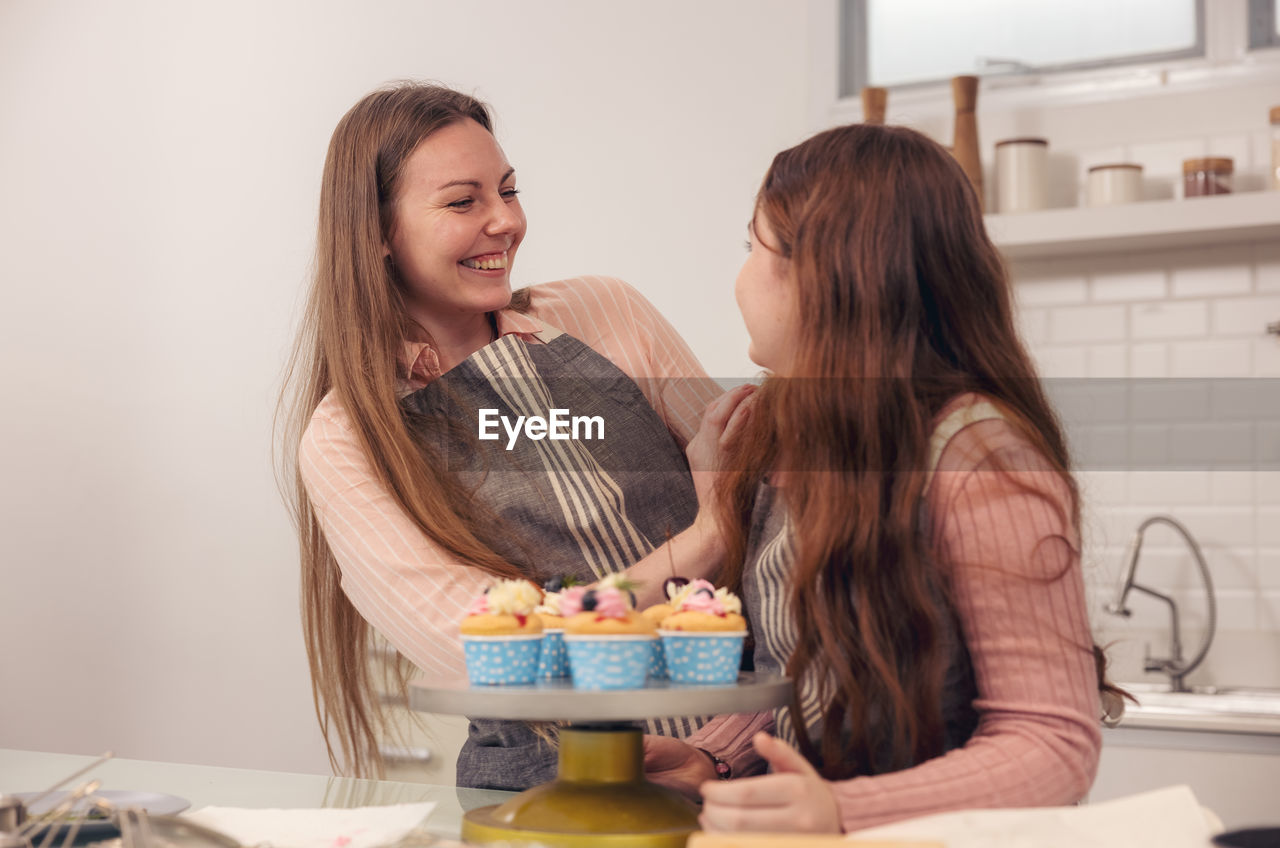 Happy family concept of a mother and her daughter enjoying cupcakes together in the kitchen at home.