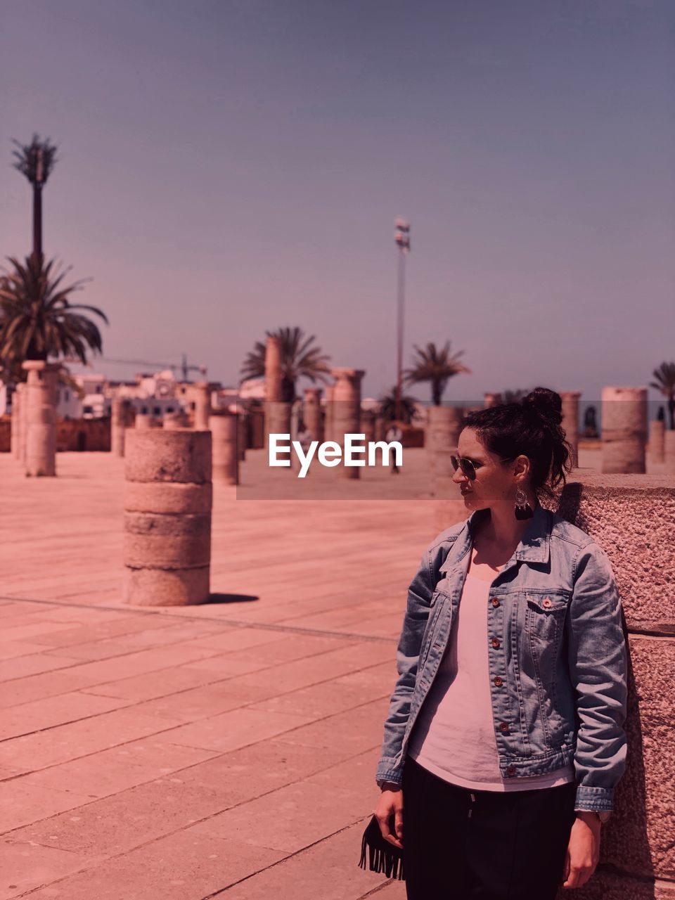 Young woman looking away while standing by stone wall against sky