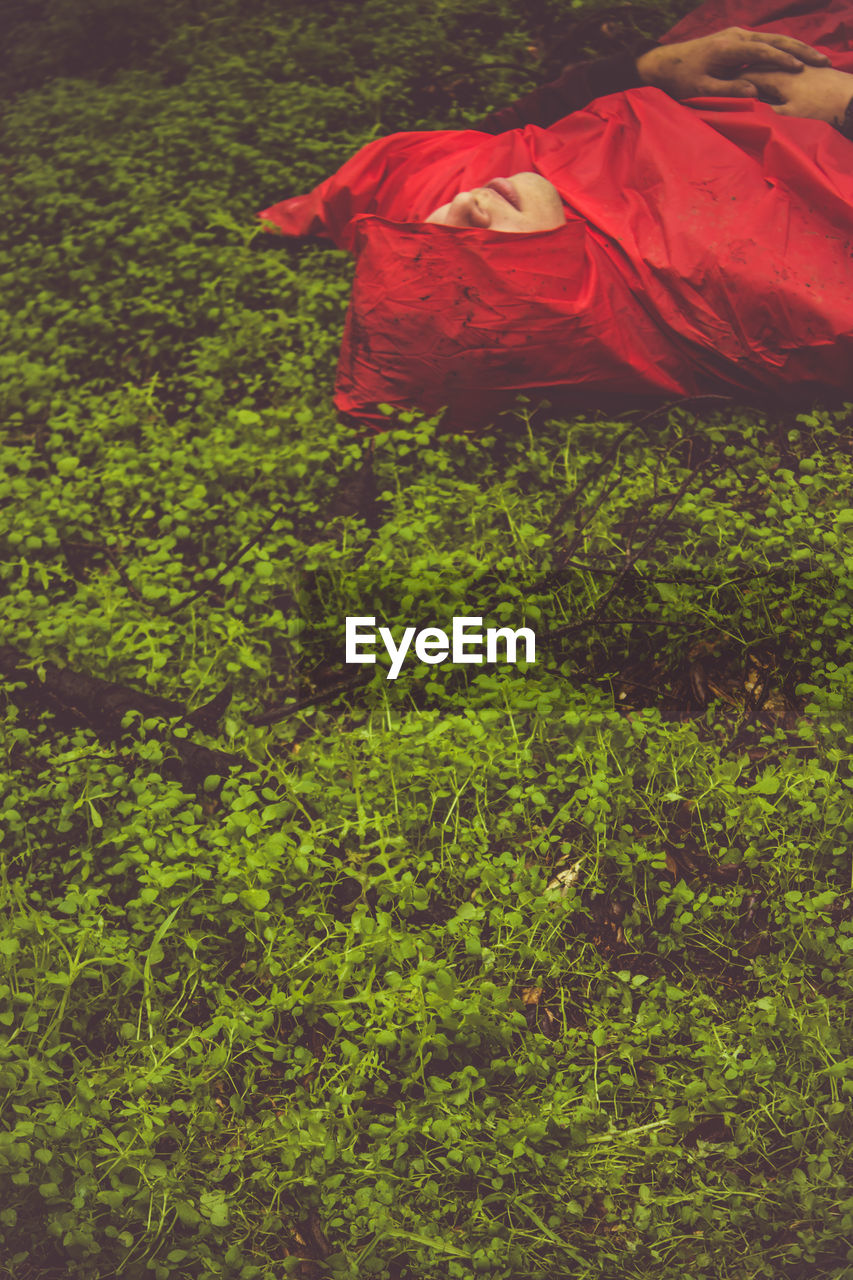 High angle view of man wearing red raincoat while lying on field