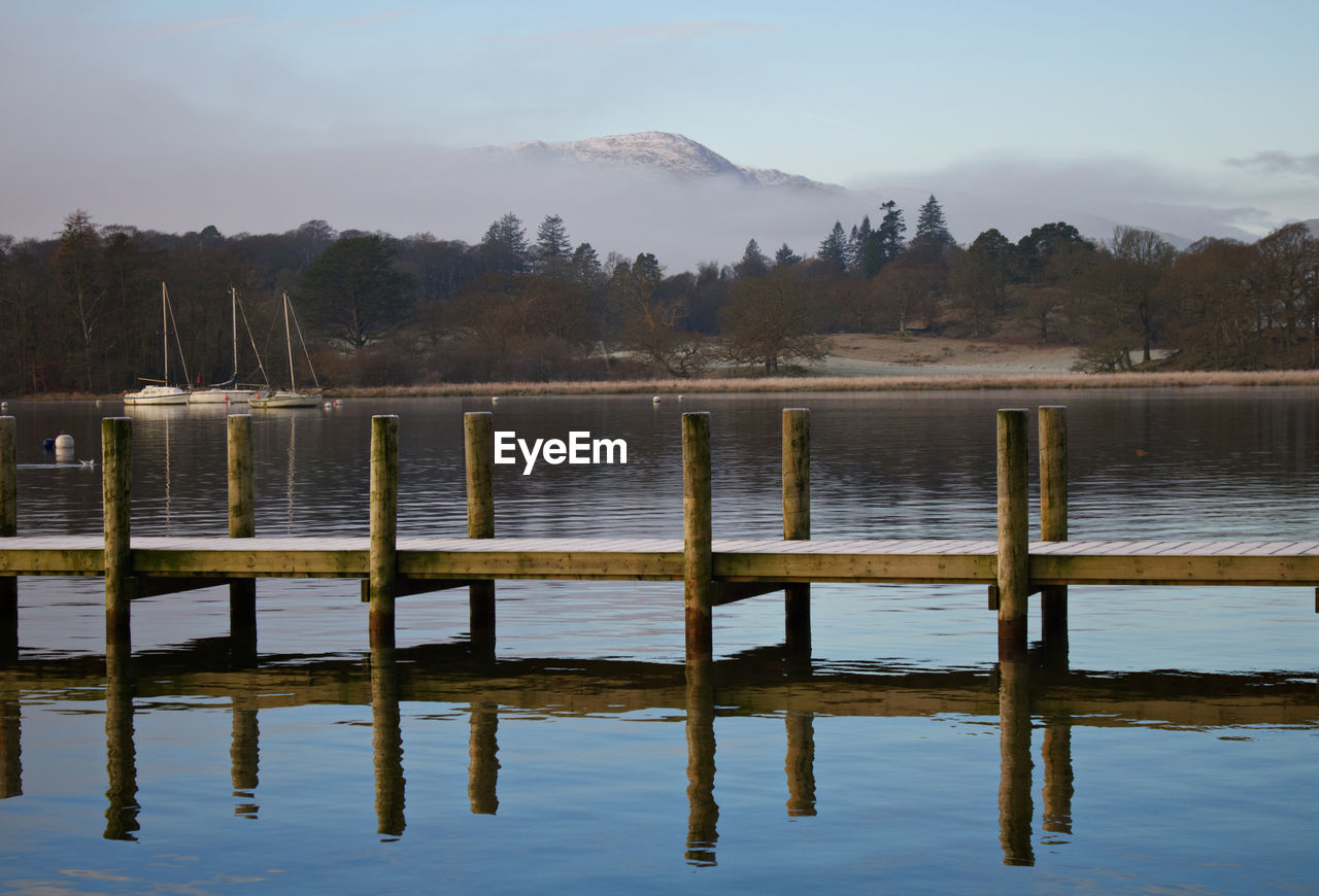 Wooden posts in lake against sky