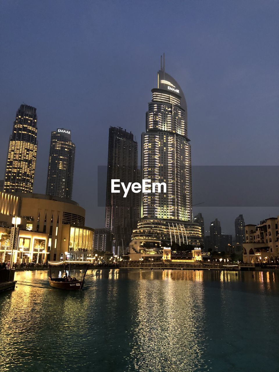 ILLUMINATED BUILDINGS BY RIVER AGAINST SKY