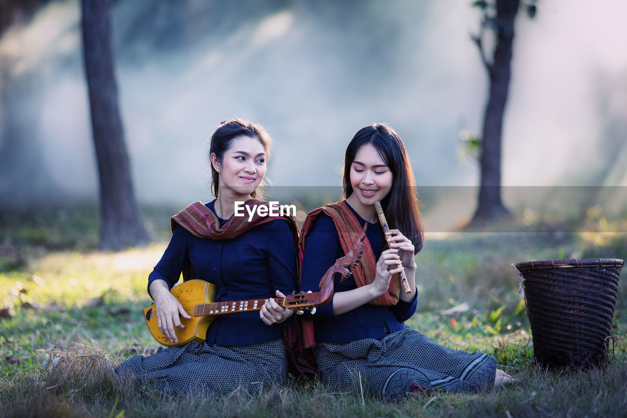 Female friends playing music while sitting on land