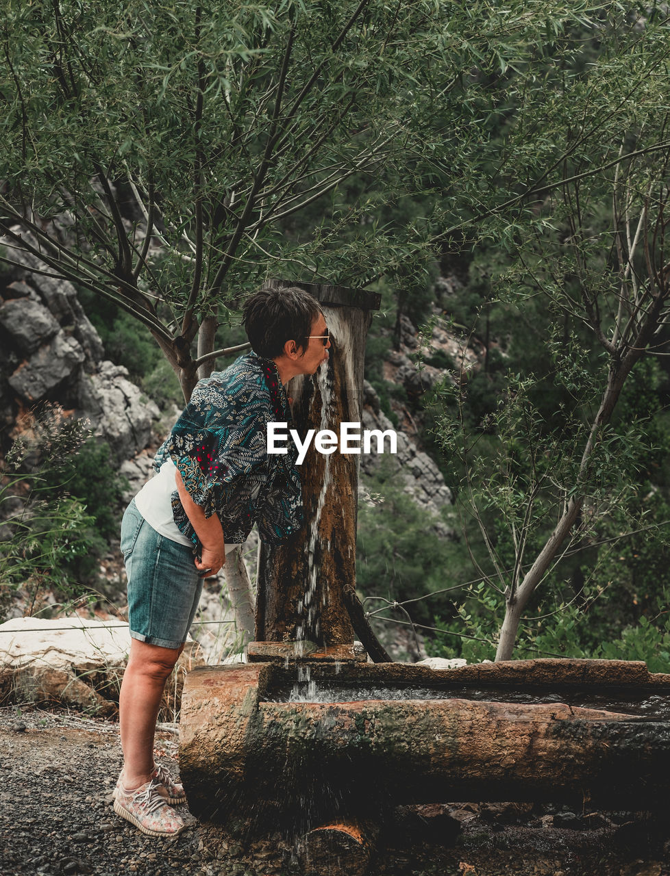 Elderly woman by the spring in the nature. senior woman drinking water from spring in the woods.