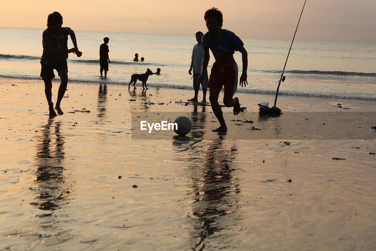 Friends playing football on beach against sky