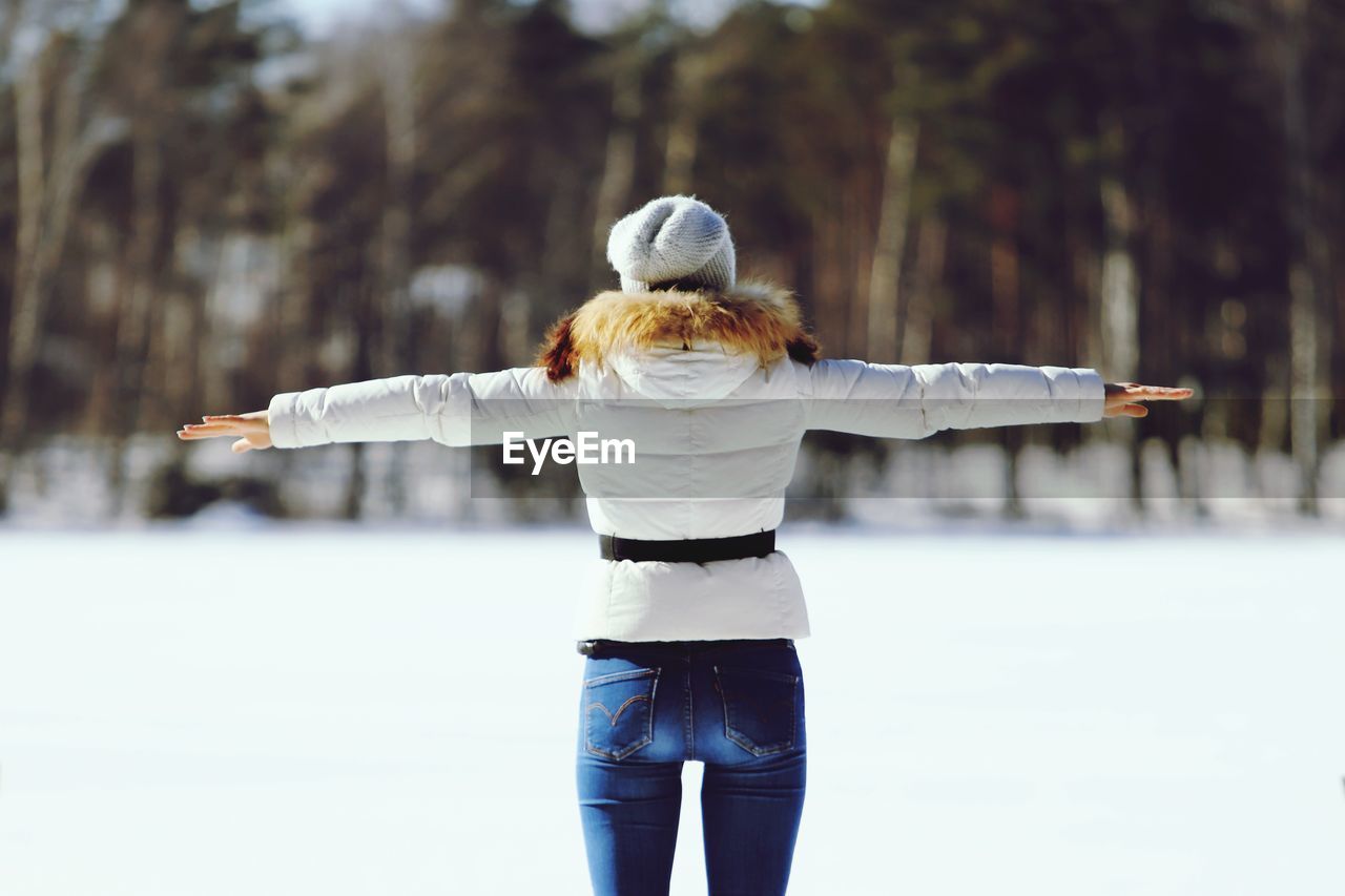 REAR VIEW OF WOMAN WITH ARMS OUTSTRETCHED STANDING IN SNOW