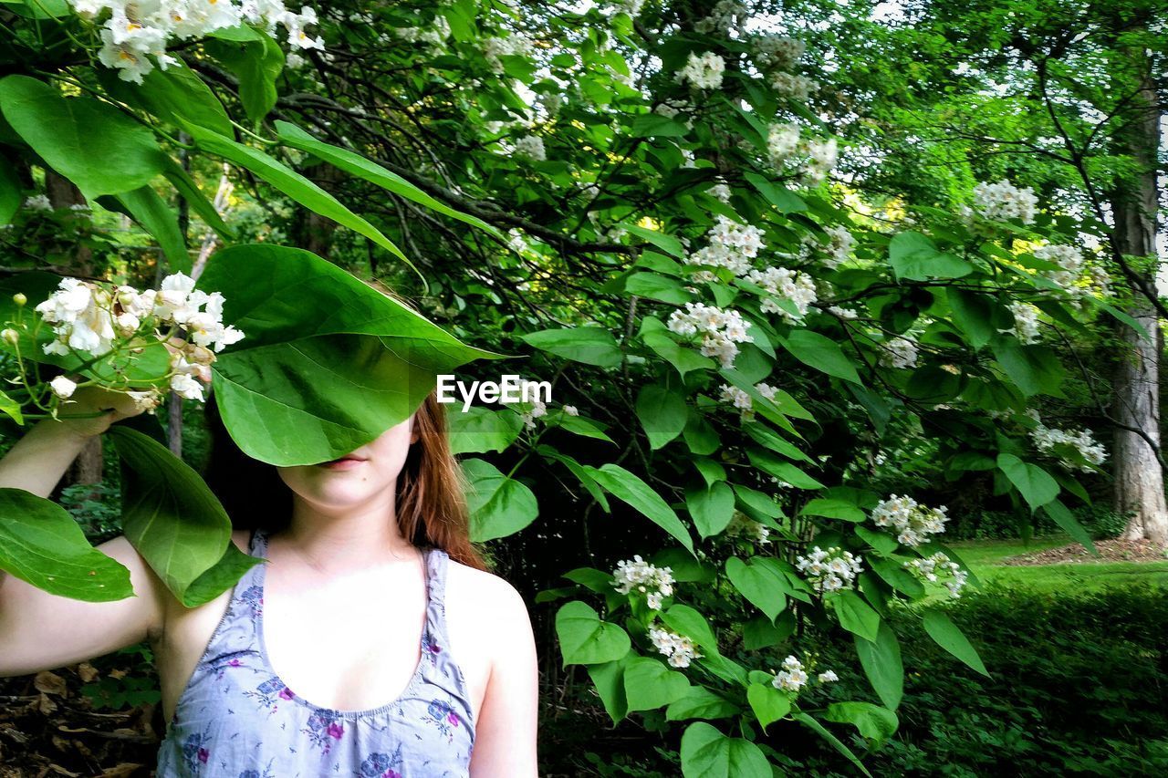 Teenage girl covering face with heart shape leaf