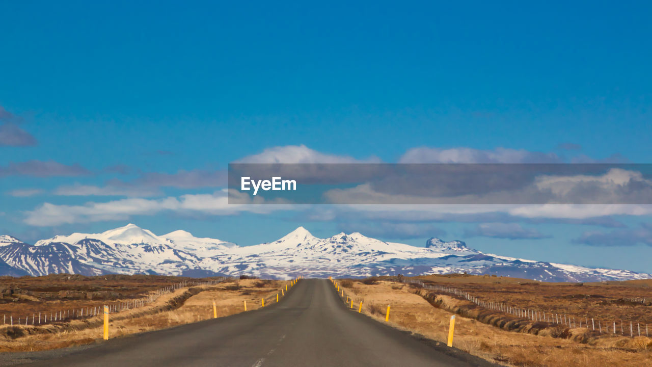 Road leading towards snowcapped mountains against sky