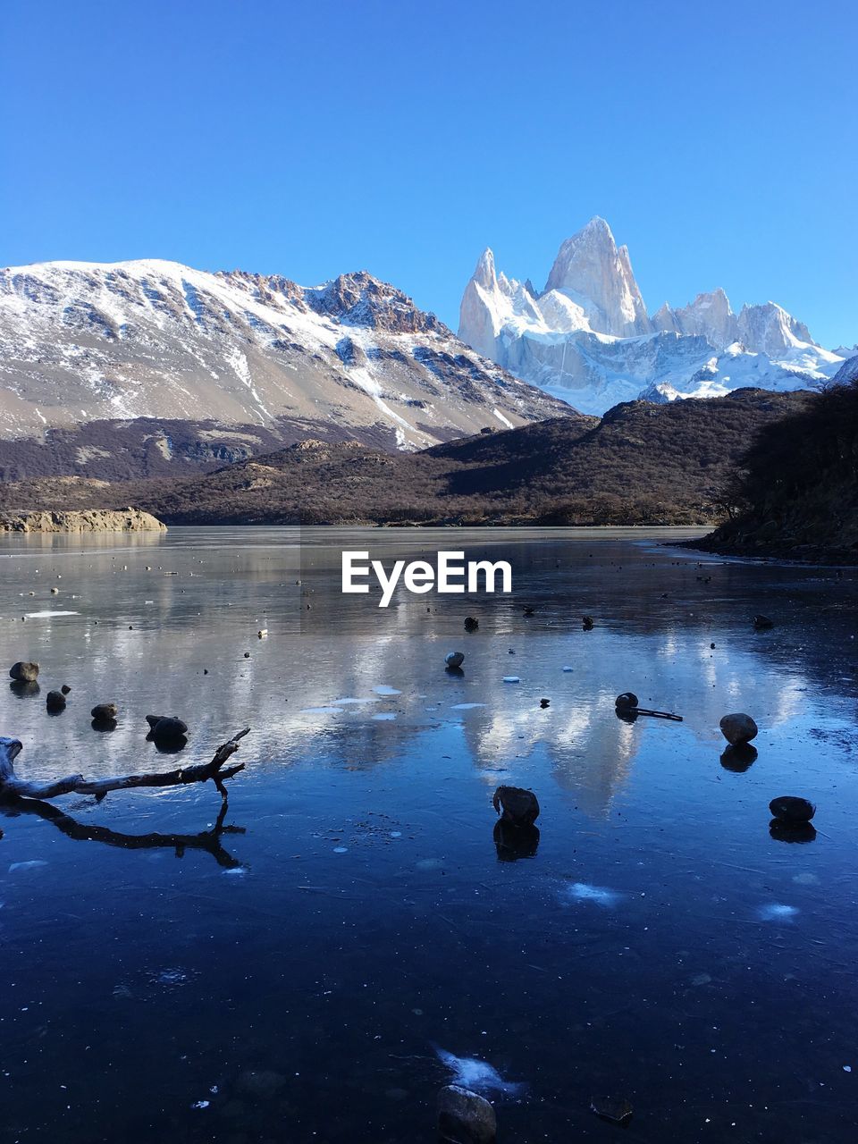 Scenic view of lake by snowcapped mountains against clear blue sky 