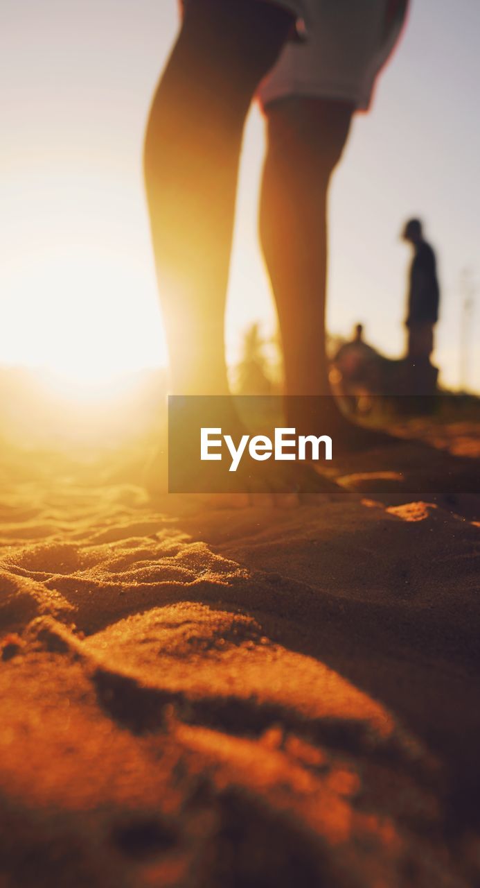 low section of man walking on sand at beach during sunset