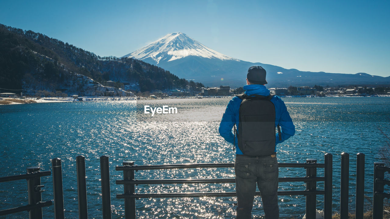 Rear view of man standing by lake against mt fuji in winter