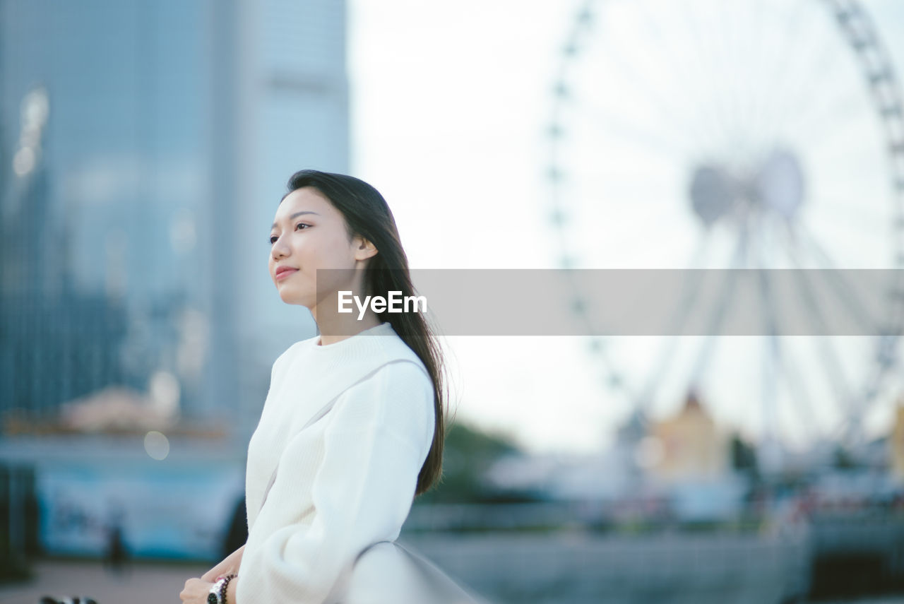 Young woman looking away while standing by railing in city