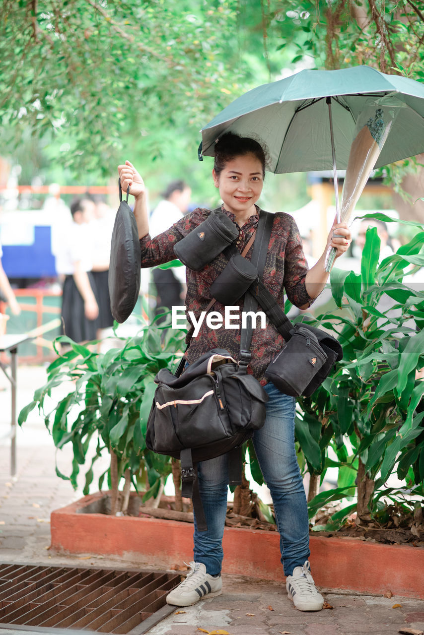 FULL LENGTH PORTRAIT OF SMILING YOUNG WOMAN STANDING ON RAINY DAY