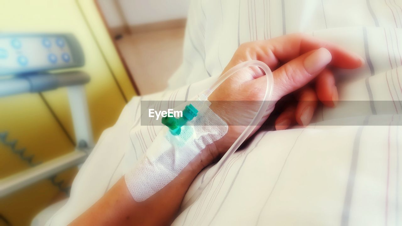 Cropped hand of woman with iv drip on bed in hospital