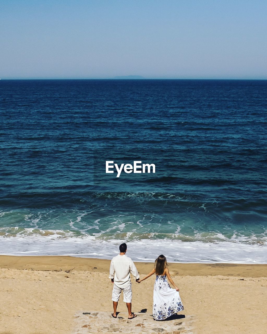 Rear view of couple on beach against clear sky