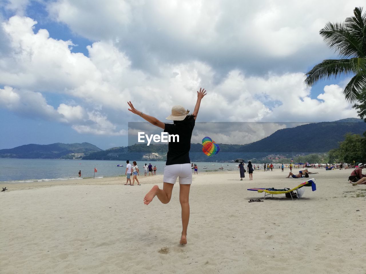 Rear view of cheerful woman dancing at beach against cloudy sky