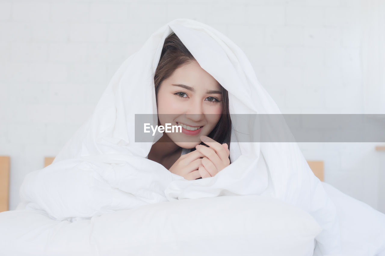 Portrait of smiling young woman sitting on bed at home