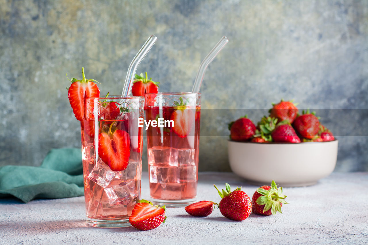 Refreshing cocktail with strawberries in glasses with a straw on the table and a bowl with berries