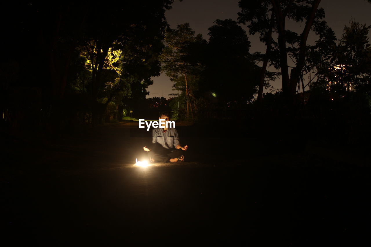 Man sitting on road against sky at night