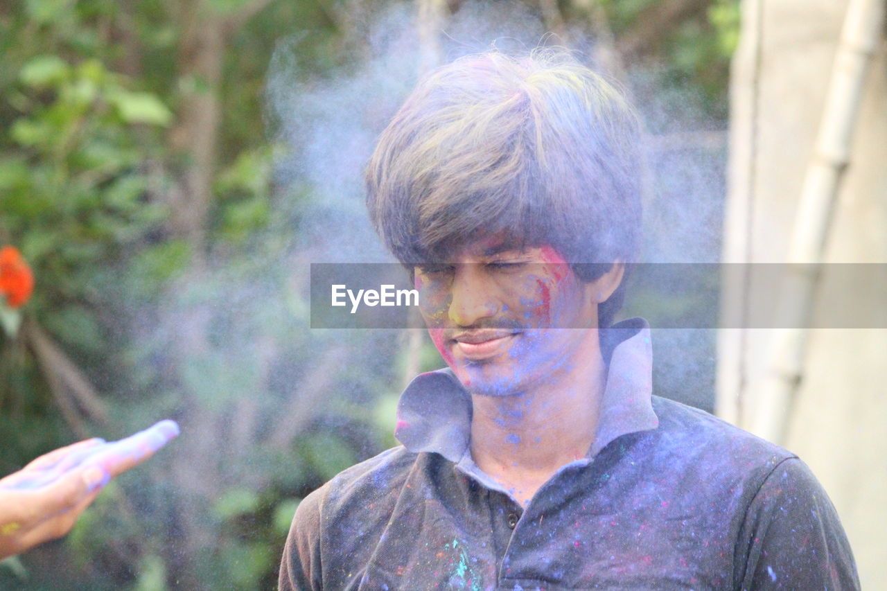 Young man with powder paint on face standing against trees at park