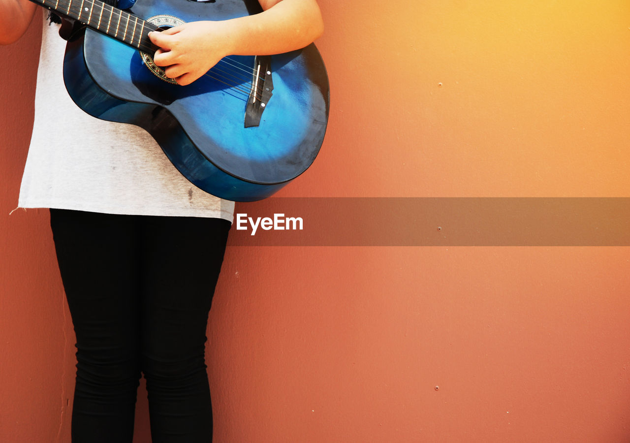 Midsection of girl playing guitar against orange wall