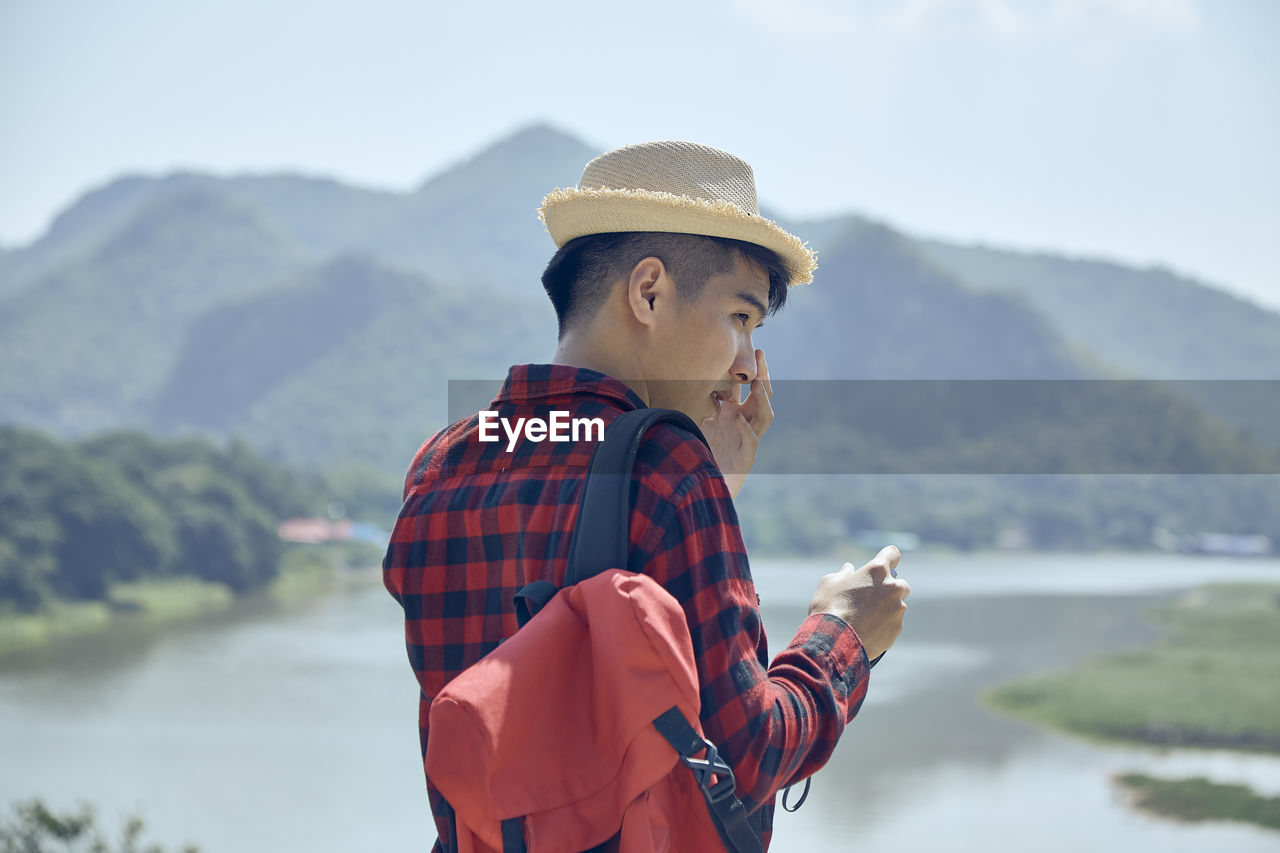 MAN WEARING HAT STANDING BY MOUNTAIN