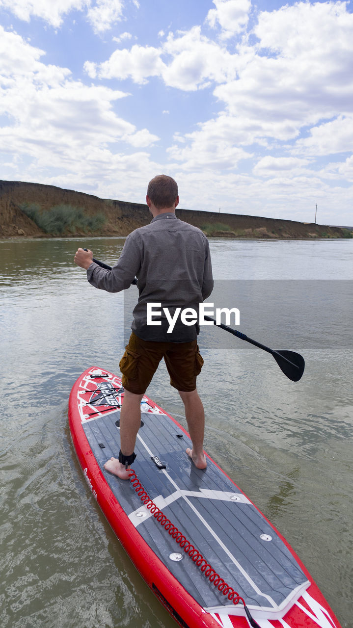 Rear view of man on paddleboard in lake against sky