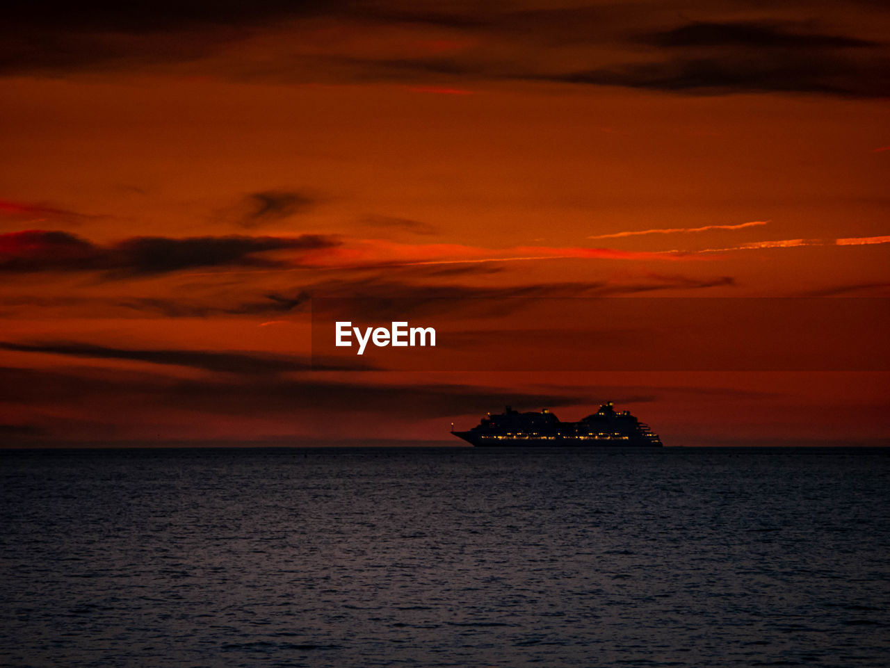 Illuminated cruise ship on the sea in front of red sky just after sunset