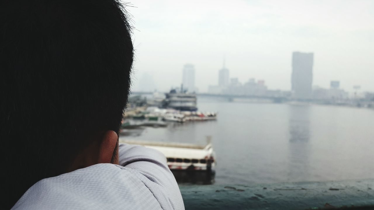 Cropped image of man by sea in city against clear sky