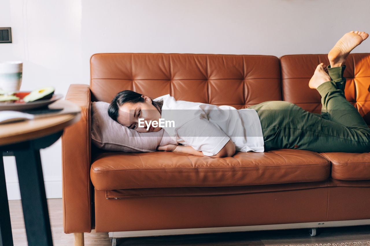 Sad brunette lies on the sofa in the living room, burnout and stress, depression and loneliness.