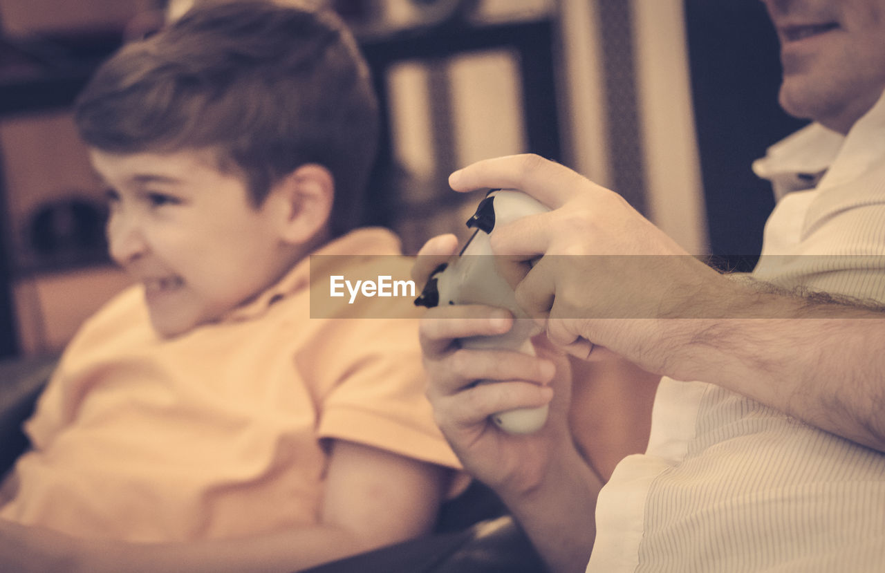 Close-up of father and son playing video games at home.