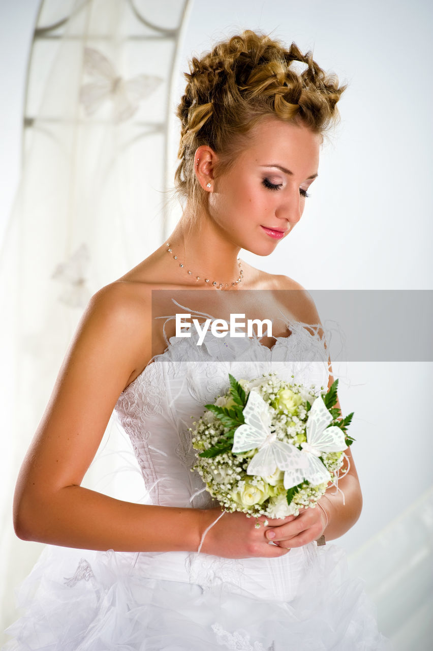 Bride with closed eyes holding bouquet while standing by arch