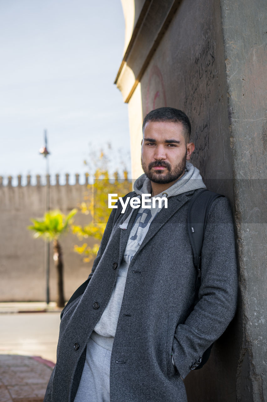 Moroccan man leaning against a wall wearing stylish grey coat