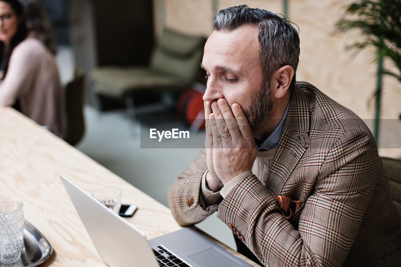 Tired businessman looking at laptop while sitting in office